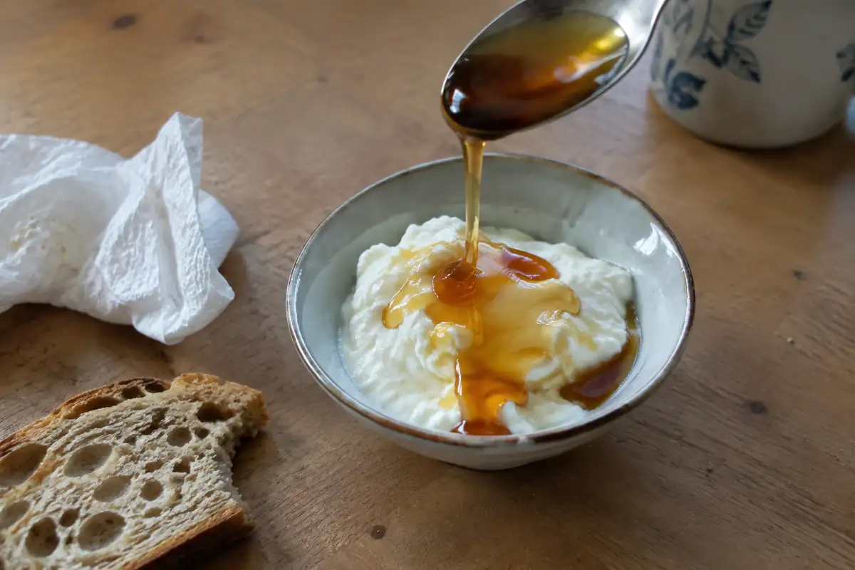 Une cuillère de miel foncé versée sur un bol de fromage blanc