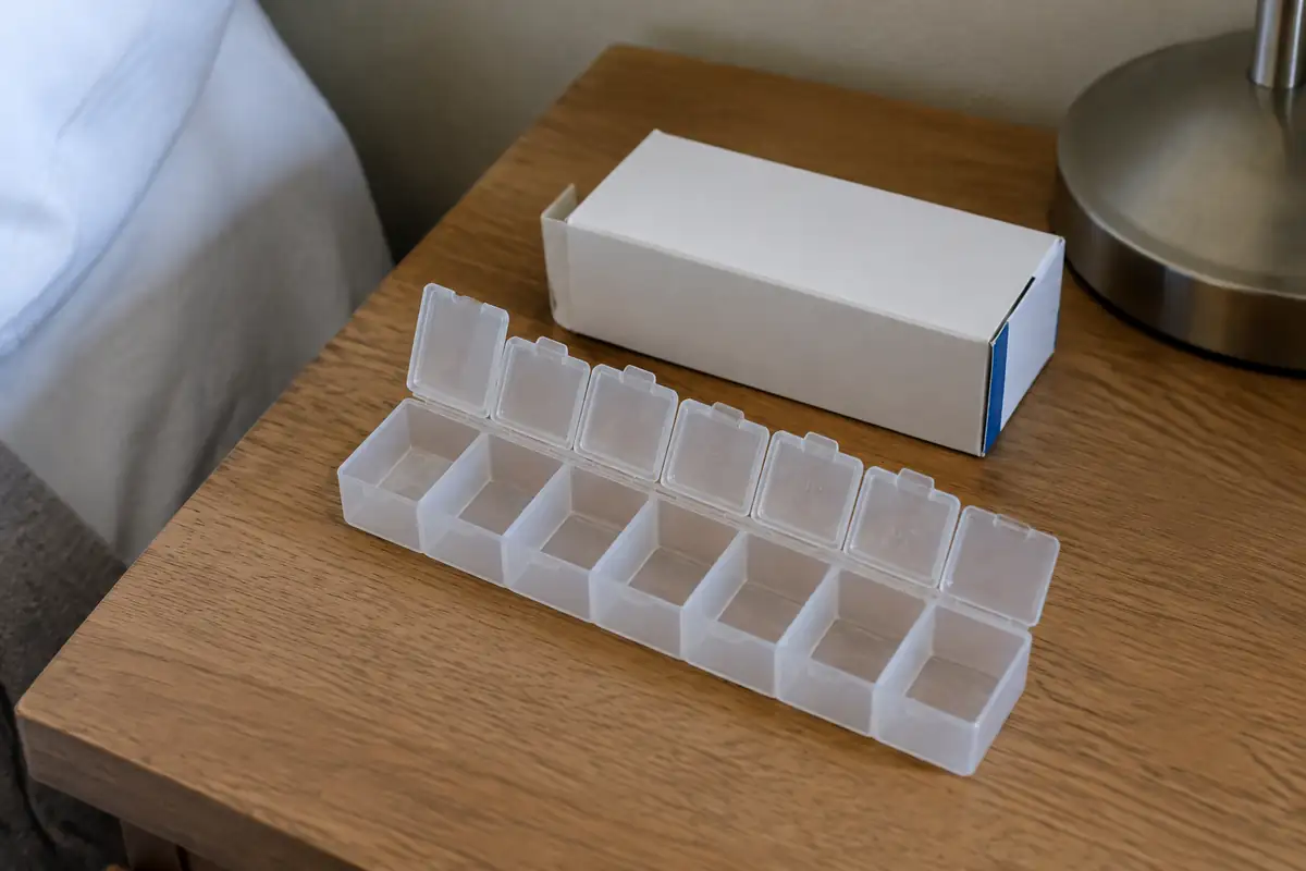 Pilulier hebdomadaire aux compartiments vides à côté d'une boîte de médicament sans étiquette, sur une table de chevet